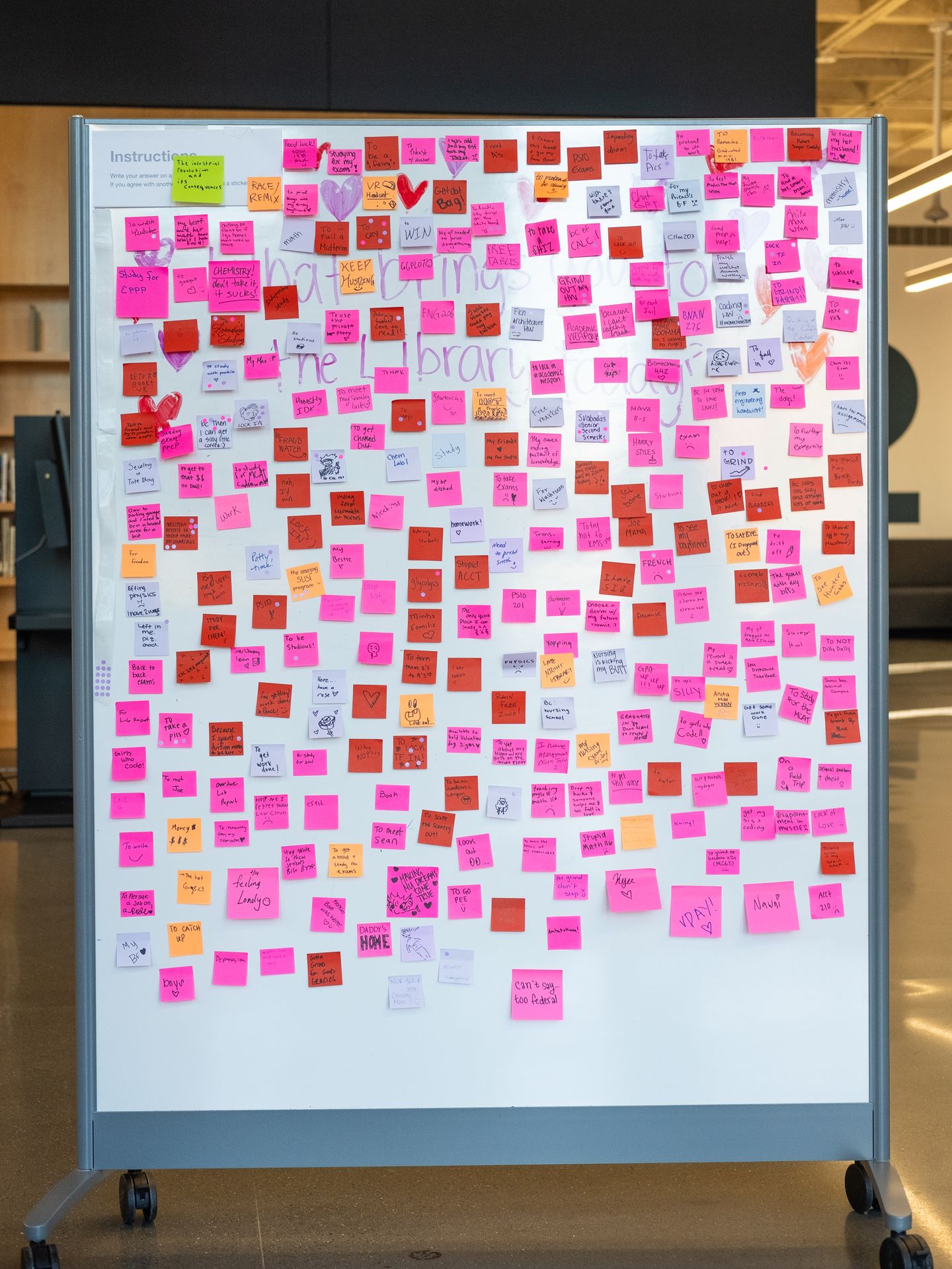 A whiteboard in an open space covered by pink and red sticky notes
