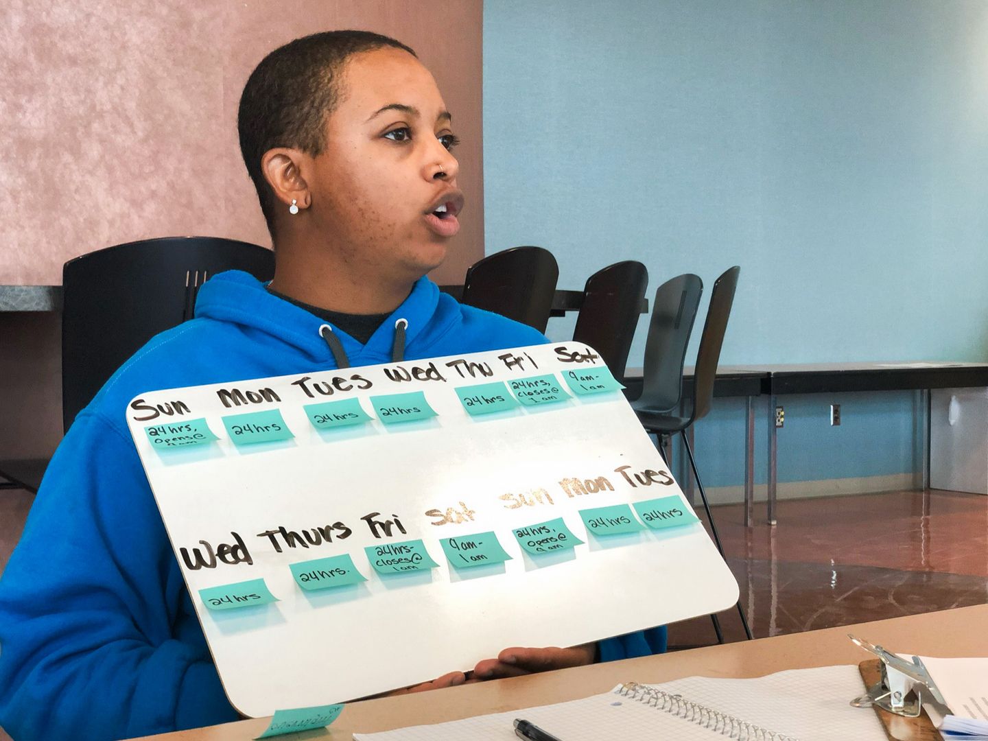 A student holding a whiteboard that has different versions of language for a weekly calendar