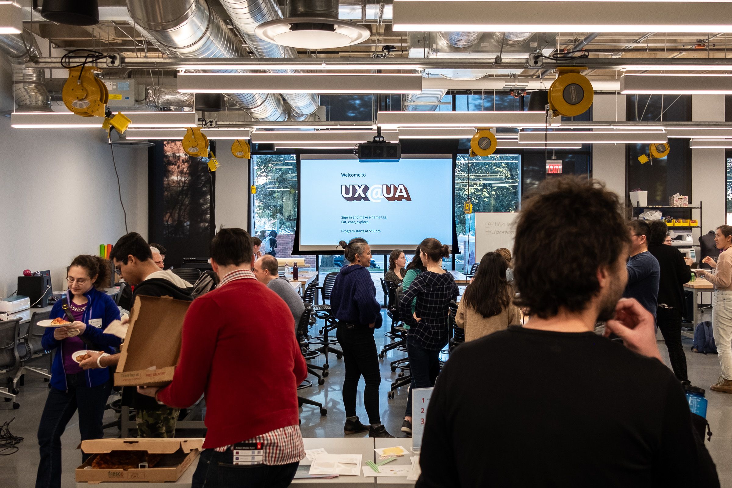 People attending a UX@UA event with the logo visible at a distance