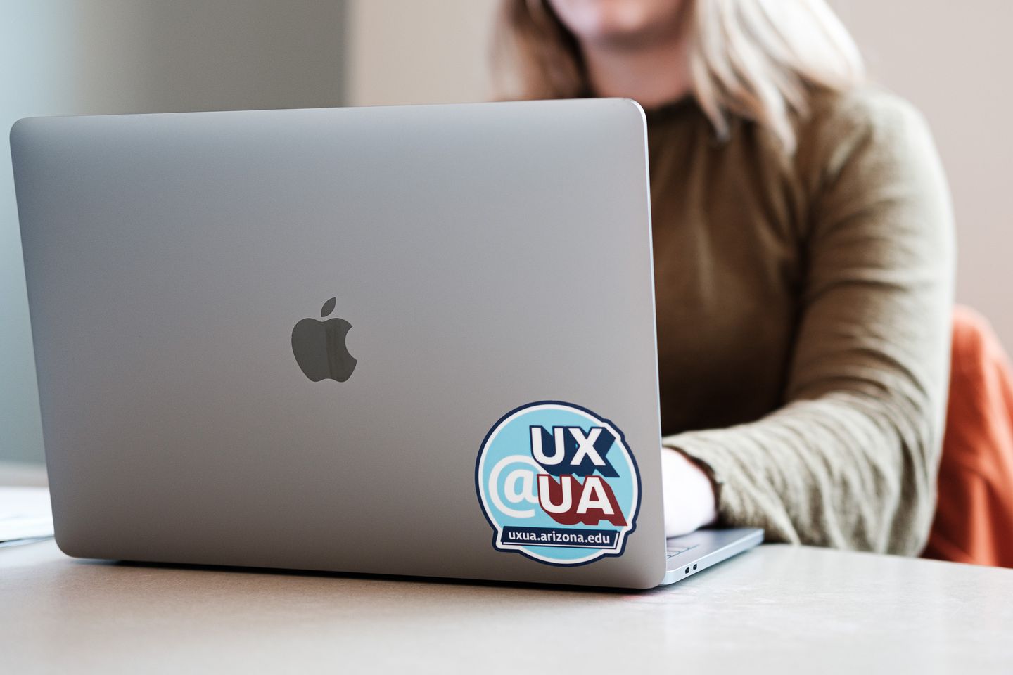 Woman using a laptop with a UX@UA sticker